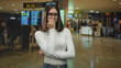 © Krakenimages.com - Young woman wearing glasses biting her nails with hand to mouth gesture in an airport terminal near departure screens and queues; travel anxiety delay.