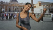 © Krakenimages.com - Thai woman wearing a striped tank top points finger with raised right arm and visible hand gesture in front of a historic building and crowded square; vacation travel playful.
