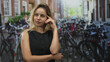 © Krakenimages.com - Woman wearing black dress with hand to forehead and arm folded across body on street in amsterdam; contemplative reflection.