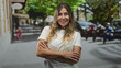 © Krakenimages.com - Middle-aged woman with arms crossed smiling on a city street beside parked scooters and trees, wearing a white t shirt and looking at camera; confidence independence.