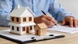 © Madison - Real estate agent signing property sale contract with client, house model on desk, mortgage loan approval concept, home buying process documentation, investment agreement signature