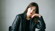 © Iconstarstudio - A stylish woman with red nails and lipstick rests her chin on her hand while wearing a black leather jacket and top.