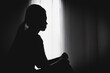 © Tinnakorn - Black and white photo. Silhouette of Teenager girl with depression sitting alone  in the dark room. Negative emotion and mental health concept.