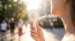 © Mariia - Woman cooling herself with a portable handheld fan during an extreme summer heatwave in the city. High temperature, hot weather, urban lifestyle, heat stress and climate change concept