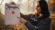 © ASHRURY - Woman holds 'November' calendar with a camera outdoors in fall foliage