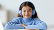 © Chandlerlikes - child with headphones smiling during online learning session, colorful pens on table, home education scene
