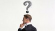 © Caleb - Young businessman in profile with large sketched question mark above head, symbolizing confusion, doubt, or seeking answers in corporate environment.