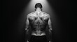 © Heshan - Shirtless muscular man with tattooed back standing in spotlight