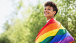 © poramin - Smiling person pride flag lgbt rainbow color outdoor happy young adult queer identity freedom confidence celebration summer nature green background community equality diversity inclusion support