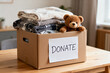© Wang - Cardboard Box Labeled Donate Filled with Folded Blankets and a Teddy Bear on Wooden Table