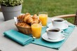 © Lubov - Two cups of coffee and basket of croissants with orange juice on table. Outdoor breakfast setting with green grass background. Morning meal enjoyed outside.