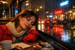 © IrenKa - Young woman resting by a rainy cafe window at night with city lights reflections, coffee cup, notebook and creative tools in a cozy urban atmosphere