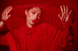 © SHOTPRIME STUDIO - Stylish woman in red outfit stands behind vibrant red fabric, creating abstract patterns. Concept of high fashion, creativity, and beauty editorial with dramatic lighting.