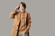 © Pixel-Shot - Stylish young man in beige coat talking by mobile phone on light background