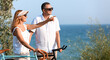© Pixel-Shot - Mature couple with bicycles walking along sea shore on summer day