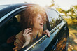 © SHOTPRIME STUDIO - Woman with curly hair leaning from a car window, smiling as she feels the breeze. Outdoors setting with warm sunlight, relaxed lifestyle, and a carefree mood.