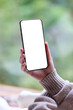 © Farknot Architect - Vertical mockup image of a woman holding mobile phone with blank white desktop screen at home