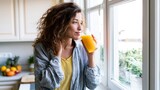 Young woman smiling and sipping fresh orange juice by the kitchen window, enjoying a healthy morning routine at home and a moment of relaxed, vibrant self care