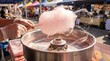 © David Zarzosa - Vendor making fluffy pink cotton candy at outdoor market fair, sweet carnival treat spinning on machine with festive summer atmosphere.