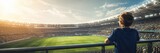 Child standing at stadium railing looking at soccer field match. Young boy fan watching game in arena. Banner with copy space