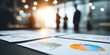 © Makmur - Business meeting with charts and graphs on table, silhouetted people in background