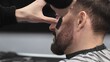 © volha_r - Professional barber performing precise beard shaving with classic straight razor, working in modern barbershop with skilled grooming technique