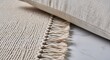 © Arnova - Close-up of a textured beige rug with fringe and a neutral linen cushion, showcasing modern living room decor elements.