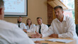 © Tania - Zero trust security architect meets with rural hospital IT team in conference room of old brick clinic building, projector casting network diagram on beige wall, three administrators with printed co