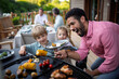 © Halfpoint - Man grilling meat and vegetable on grill during family summer garden party.