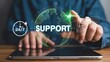 © ShepraRani - Man touching glowing global support icon on virtual screen with tablet and 24/7 clock.