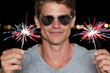 © whitestorm - Man wearing sunglasses smiling and holding sparklers with red, white, and blue lights at night
