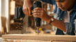© Elvira - Young woman using a cordless power drill on a wooden plank in a workshop