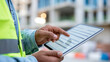 © Nataliya - Close-up of an engineer's hands holding a tablet displaying digital inspection forms at a construction site, digital site management concept, construction technology photography,