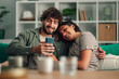 © Zamrznuti tonovi - Happy couple relaxing on sofa sharing smartphone content, smiling while enjoying social media and connection at home
