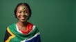 © BETTOVERSE - Proud South African woman with face painted in national colors and draped in the flag, smiling against a green studio background