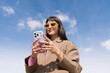 © JORGE PONZ/Stocksy - Bright spring day with a young woman using her phone outdoors