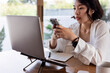 © Jovo Jovanovic/Stocksy - Woman using phone while working on laptop at desk.