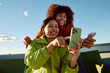 © Edu Bastidas + David Garcia/Stocksy - Women using smartphone together on rooftop smiling and sharing