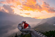 © Kittiphan - Female tourist in long red dress enjoying the dramatic golden hour view on a giant hand viewpoint in Sapa, Vietnam