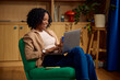 © Boris Jovanovic/Stocksy - Woman uses her laptop while seated in a green chair.