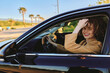 © SHOTPRIME STUDIO - Smiling woman with curly hair driving a sleek car under bright sunlight, palm trees in the background. Casual lifestyle shot highlighting freedom, travel, and everyday moments captured with warm