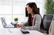 © David - Smiling asian businesswoman managing tasks, using smartphone and laptop, analyzing financial documents, working efficiently at modern office workspace