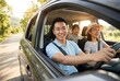 © Olga Ко - Happy Asian family enjoying a summer road trip, smiling father driving a car with wife and little daughter, looking out the window, travel concept