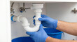 © Janna - Plumber adjusting P-trap under bathroom sink with gloves