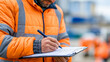 © Nataliya - Faceless safety officer writing notes on a permit-to-work form at a defocused construction site, safety permit, job hazard analysis, risk assessment documentation, site
