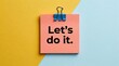 © Drago Designer - Motivational sticky note with Let's do it text, pink adhesive memo on yellow and blue background, inspirational message for business productivity