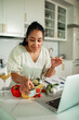 © Marko Geber - Woman preparing vegetables while following an online recipe on a laptop in a home kitchen
