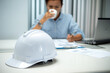 © Chaiphorn - White safety helmet on desk with female engineer working in office construction concept