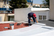 © Ladanifer - Construction worker applying a white waterproof membrane on a red flat roof during renovation