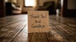 © Mudassir - Brown paper note featuring handwritten thank you and goodbye message resting on rustic wooden floorboards in a warm home interior